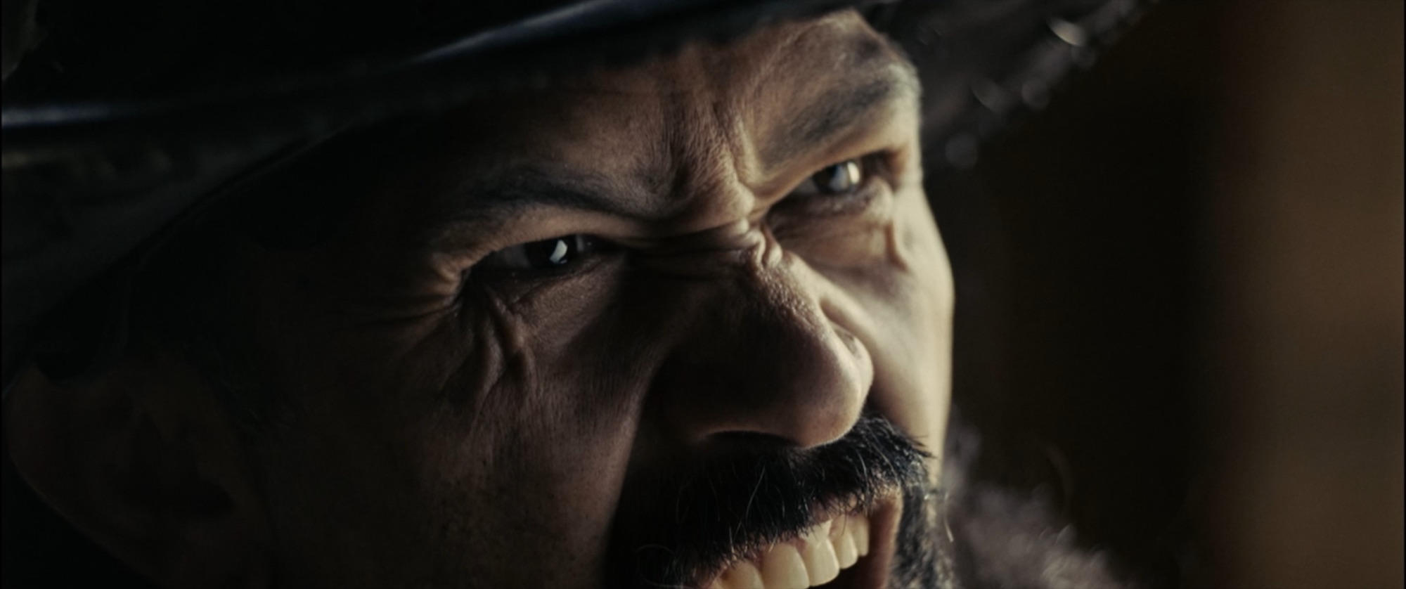 Extreme close-up of a weathered man's face under a hat brim, teeth bared in a snarl - Amon Amarth